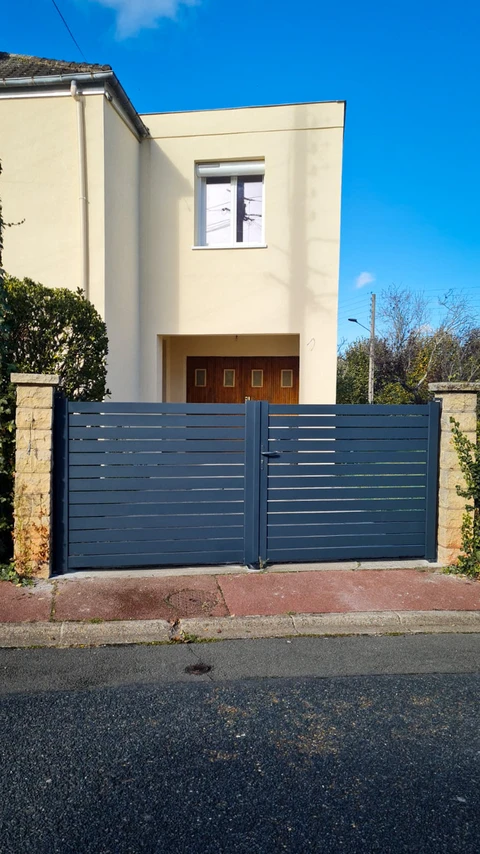 Portail double battant en aluminium laqué gris anthracite, à lames horizontales espacées, monté sur piliers en pierre calcaire