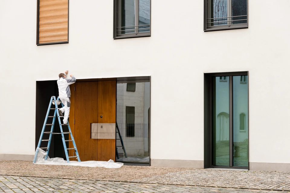 Artisan en tenue blanche travaille sur échelle devant façade moderne