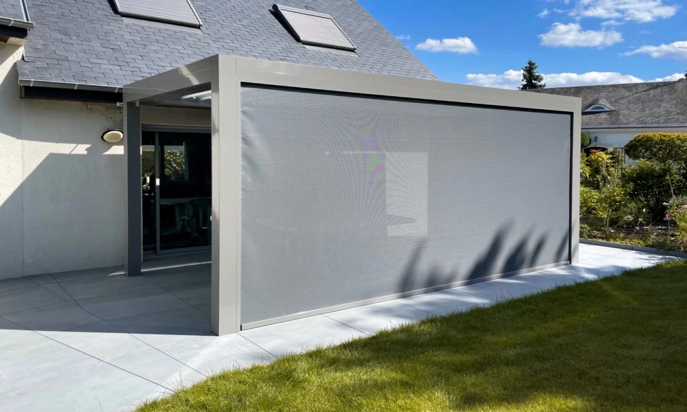 Terrasse extérieure moderne avec pergola bioclimatique aluminium laqué gris clair, store screen latéral toile microperforée gris anthracite en position déployée, fixé sur cadre aluminium