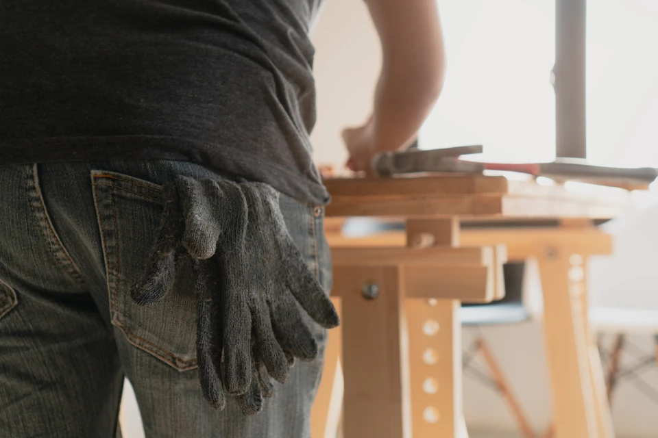 Photographie d'un artisan menuisier en tenue professionnelle discutant avec un client dans un atelier ou showroom, tous deux examinant des échantillons de fenêtres, portes ou volets. L'image doit mettre en avant la relation de confiance et l'accompagnement personnalisé du client par le professionnel, avec des produits de menuiseries extérieures visibles ou partiellement visibles en arrière-plan.