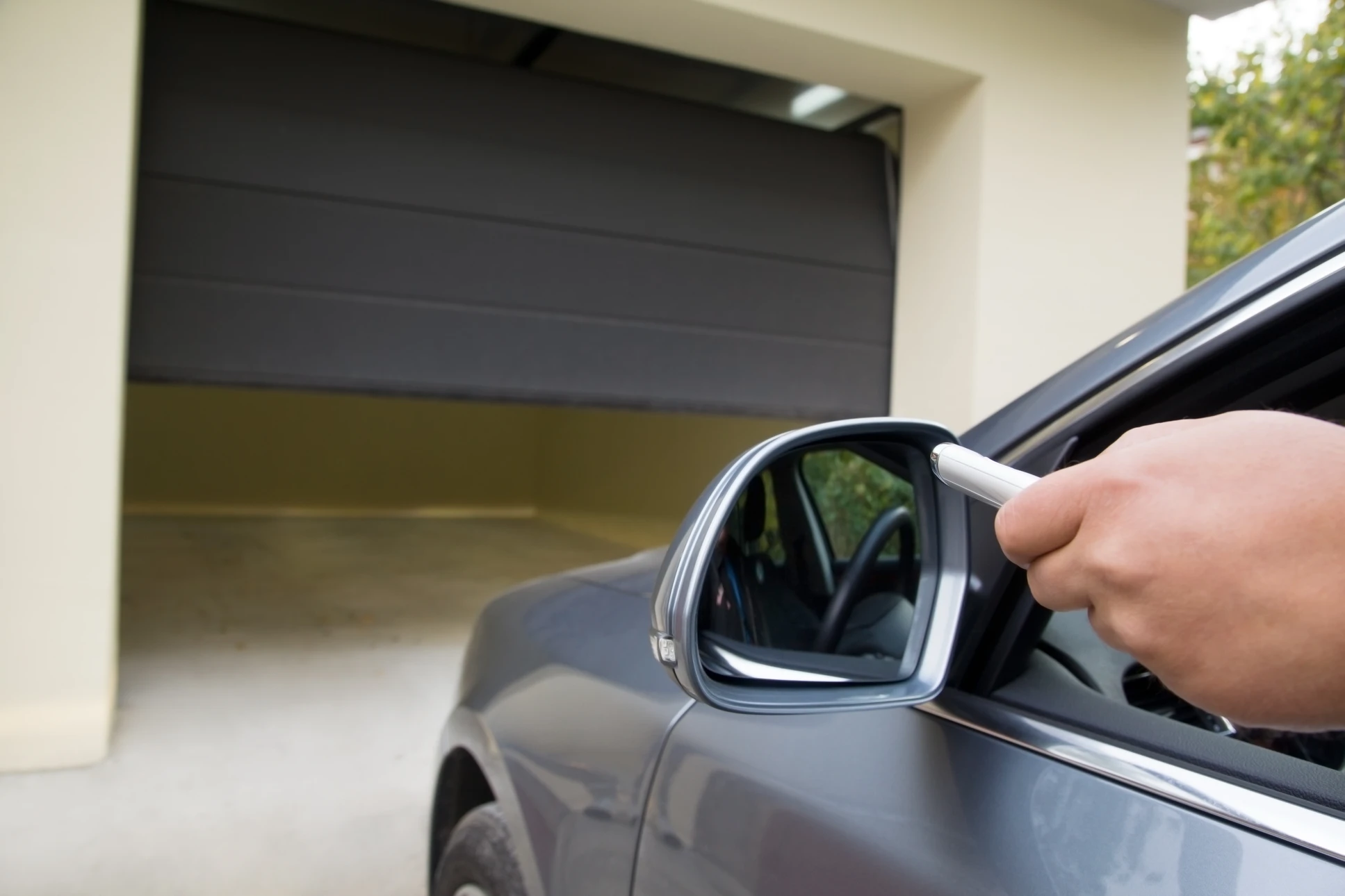 Conducteur dans véhicule gris utilisant télécommande pour ouvrir porte de garage résidentiel