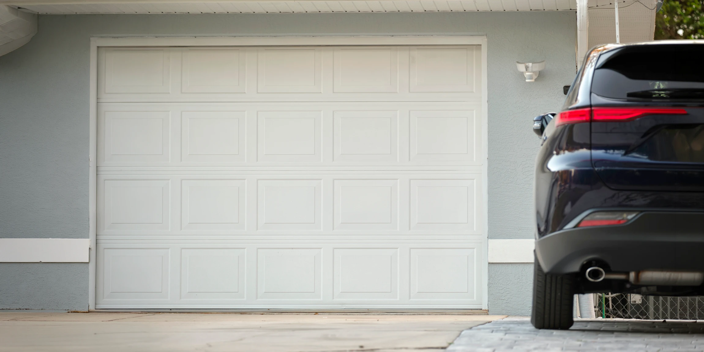 Deux techniciens en combinaison orange et noire installent une porte de garage sectionnelle blanche dans un garage résidentiel